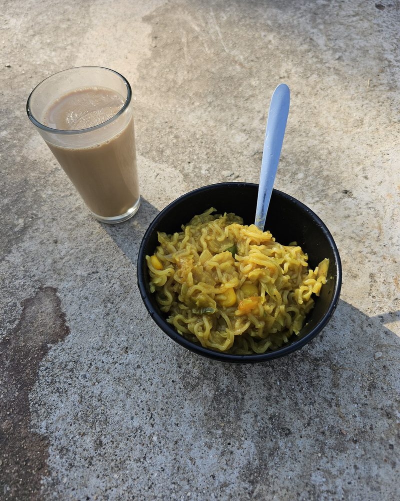 A bowl of Maggi noodles beside a glass of masala chai on a stone ledge